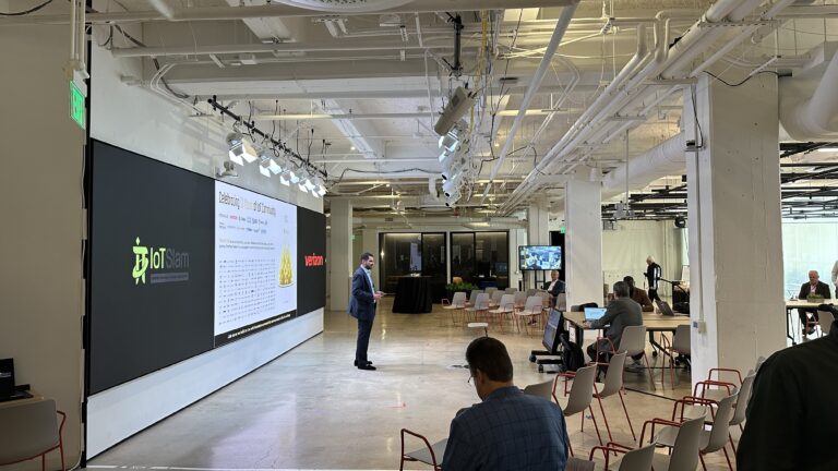 A speaker addresses the room beside a slide celebrating ten years of the IoT Community.